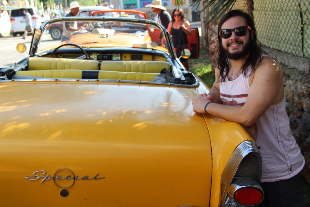 a man leaning on a yellow convertible car