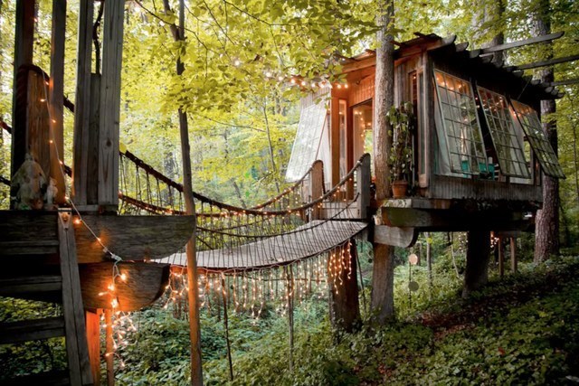 a tree house with lights from a rope bridge