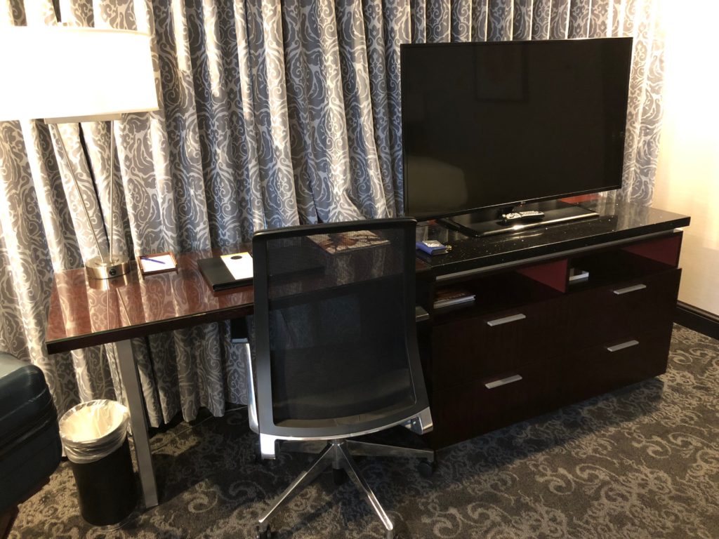 a desk with a tv and a chair in front of a curtain