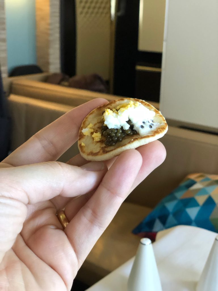 a hand holding a small cracker with black caviar and eggs