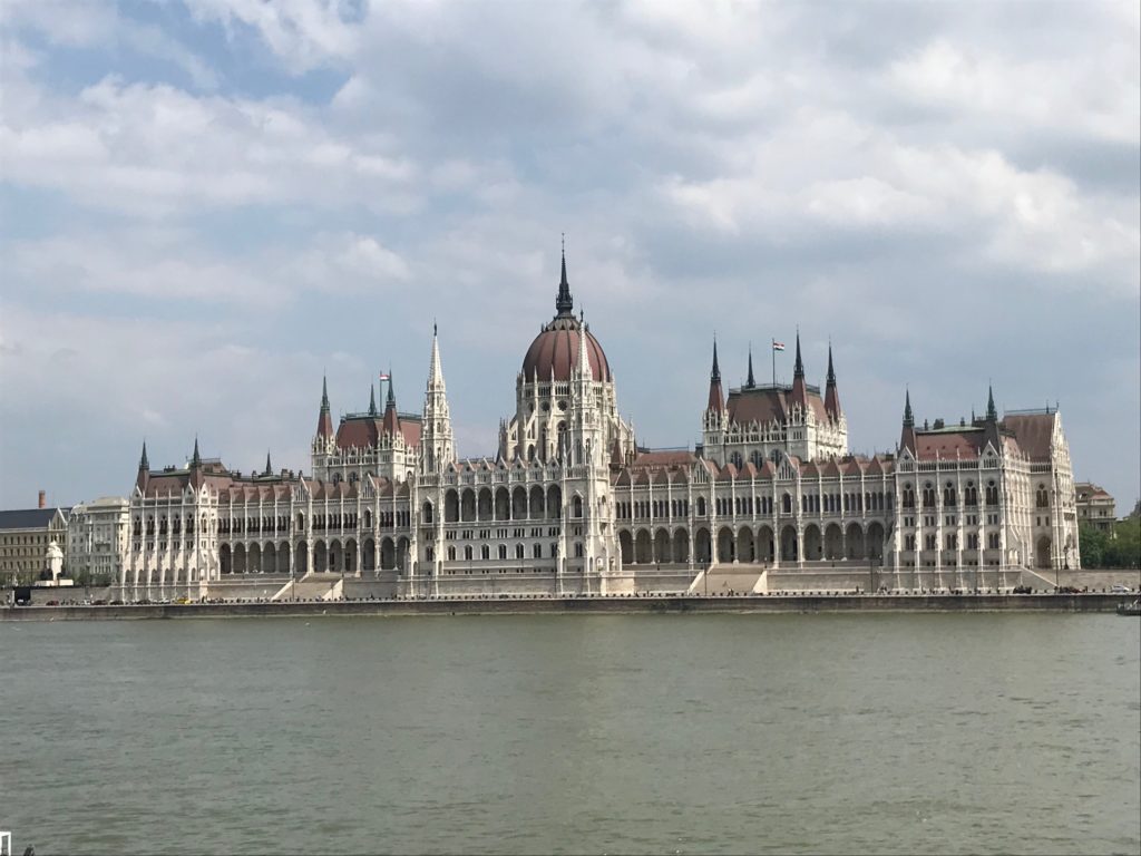 a large building with a domed roof and a body of water with Hungarian Parliament Building in the background