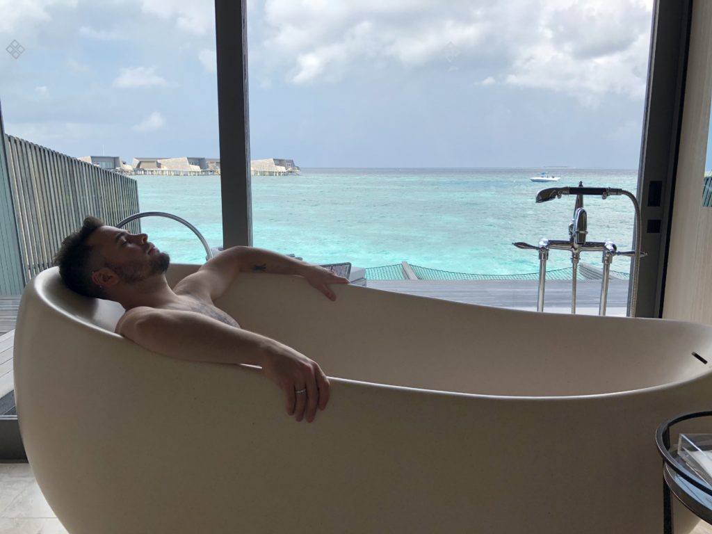 a man lying in a bathtub with a view of the ocean