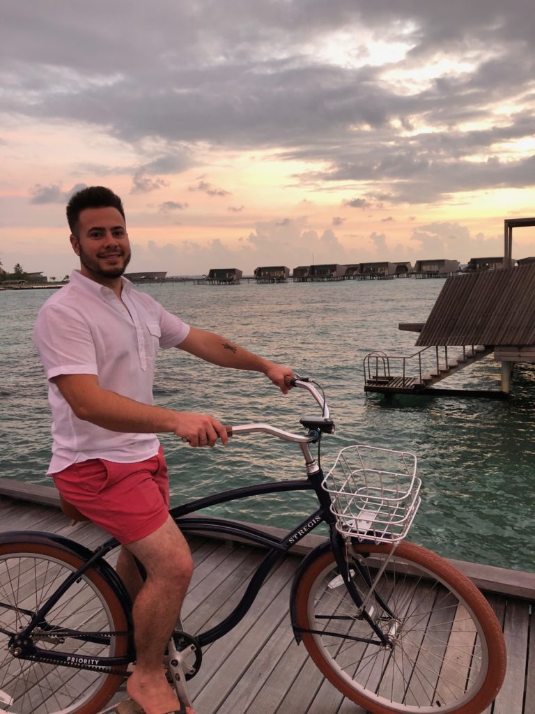 a man on a bicycle on a dock with water and buildings in the background