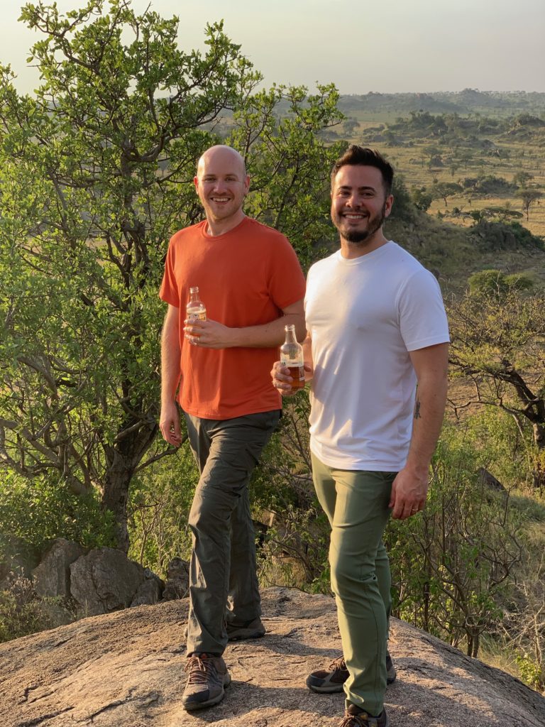 two men standing on a rock holding bottles of beer