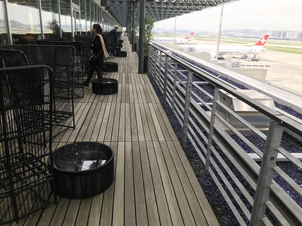 a wooden deck with metal chairs and a woman walking