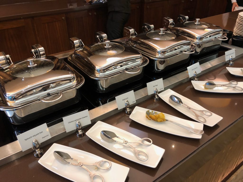 a row of silver containers with lids and spoons on plates