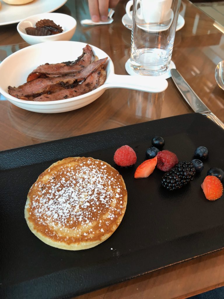 a pancake with berries and a bowl of bacon