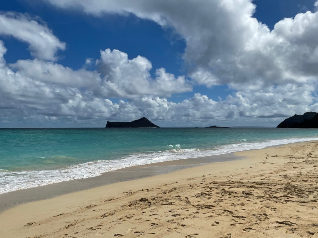 a sandy beach with blue water and island in the background