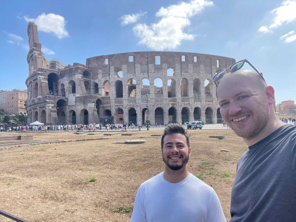 two men taking a selfie in front of a large stone building