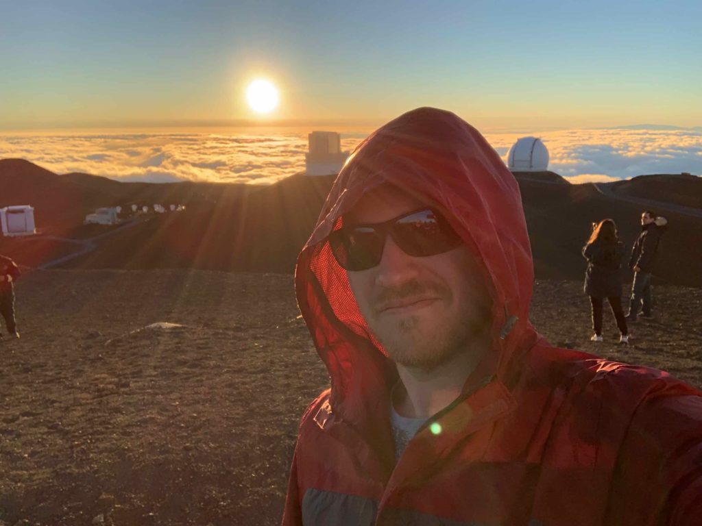 a man taking a selfie with a sunset over the clouds