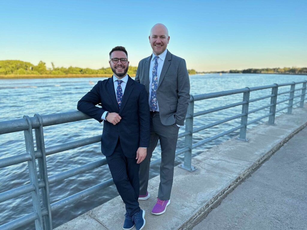 two men in suits standing on a railing next to water